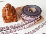 3 Webbandrollen mit dem Sanskritzeichen "Om" und eine mit Yogafiguren und eine schmale mit Herzchen jeweils in grau mit blassrosa  liegen neben einer Buddafigur aus Holz