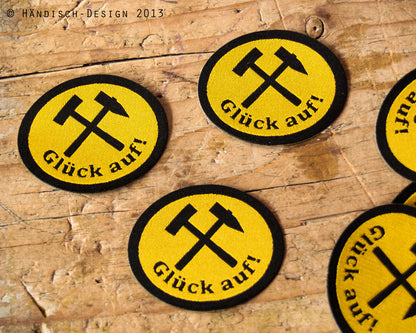 3 ovale Aufnäher mit dem Spruch Glück auf und Schlägel und Eisen in schwarz mit gelb.