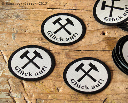 3 ovale Aufnäher mit dem Spruch Glück auf und Schlägel und Eisen in schwarz mit weiß.